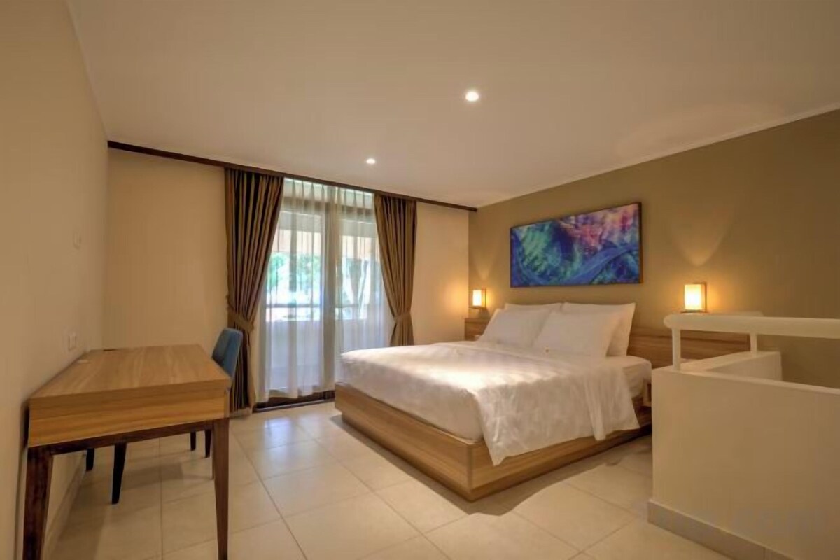 A hotel room with a bed, a desk, and a window with curtains.