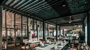 An indoor dining area with tables and chairs, large windows, and a ceiling with a grid-like pattern. - Mambruk Hotel & Convention (Anyer)