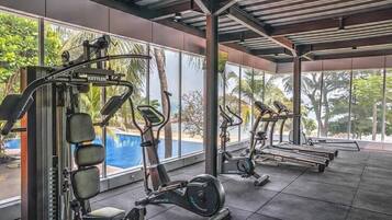 Une salle de sport équipée de machines de cardio, de machines de musculation et offrant une vue sur une piscine.