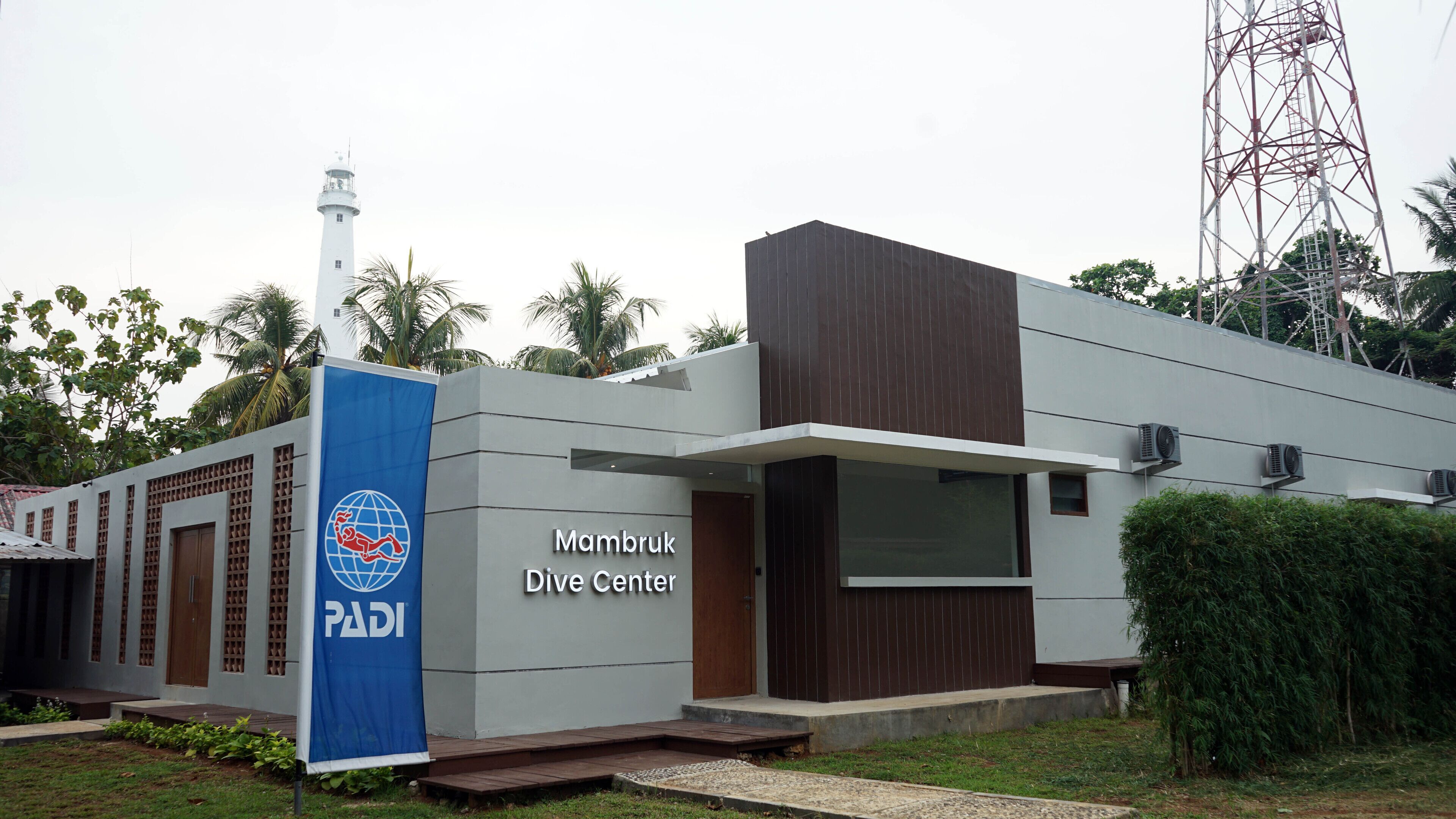 Ein modernes Gebäude mit der Aufschrift „Mambruk Dive Center“, mit einer blauen Flagge, die einen Globus und einen Taucher zeigt.