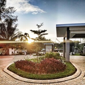 A landscaped area with a circular garden bed, a paved walkway, and a building with a modern design. - Mambruk Hotel & Convention (Anyer)