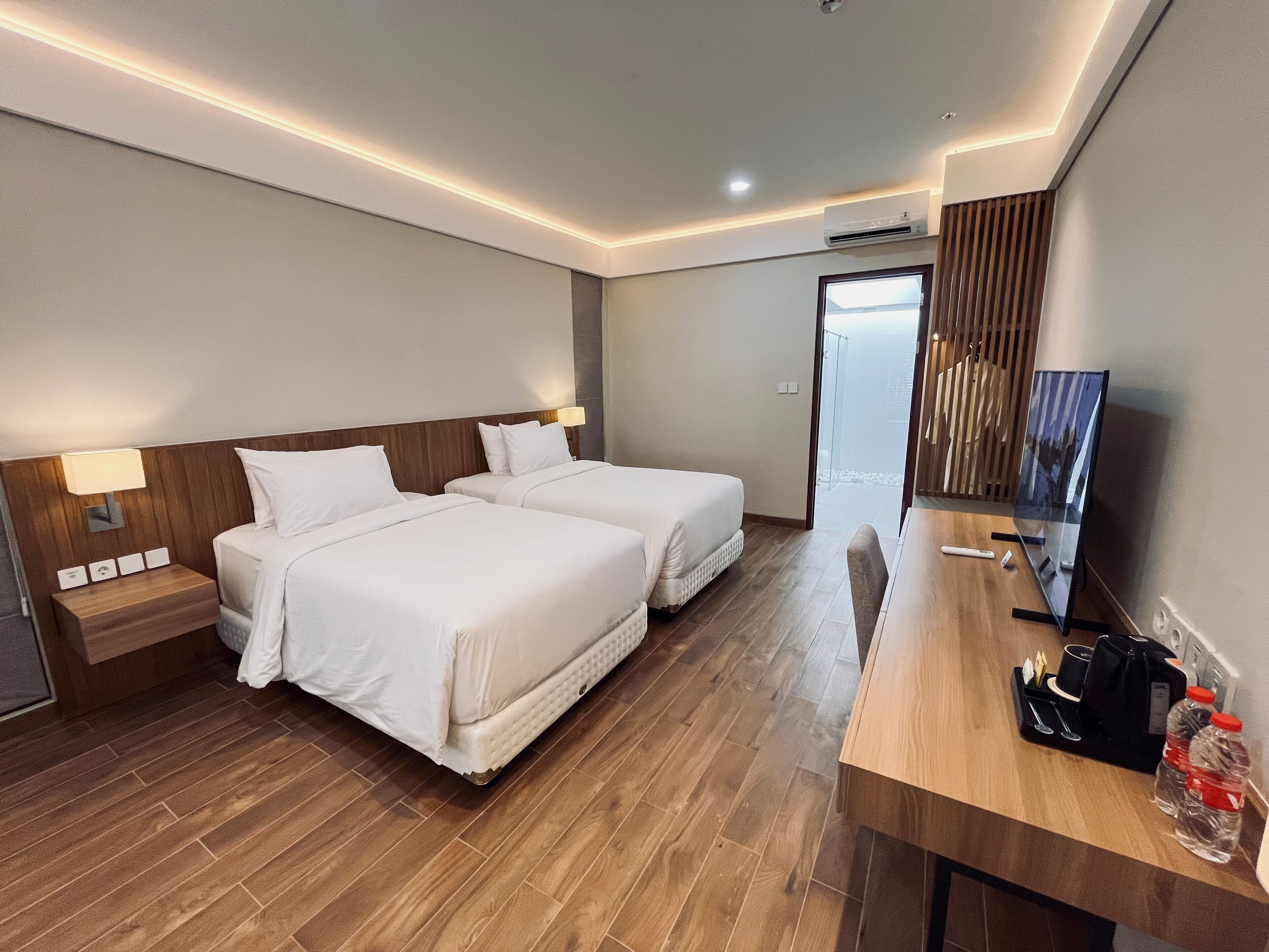Habitación de hotel con dos camas, un escritorio de madera, televisión y vista a la ciudad.