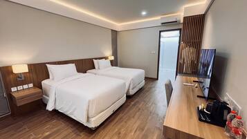 Habitación de hotel con dos camas, un escritorio de madera, televisión y vista a la ciudad.