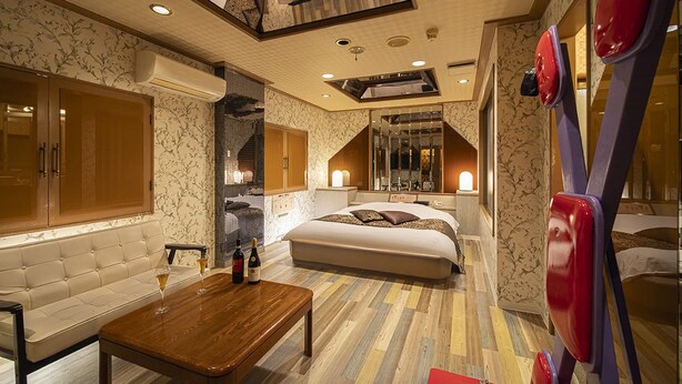 A hotel room with a large bed, a sofa, a wooden coffee table, and a mirror. - Hotel Jardin de Fleurs - Adult Only (Kyoto)