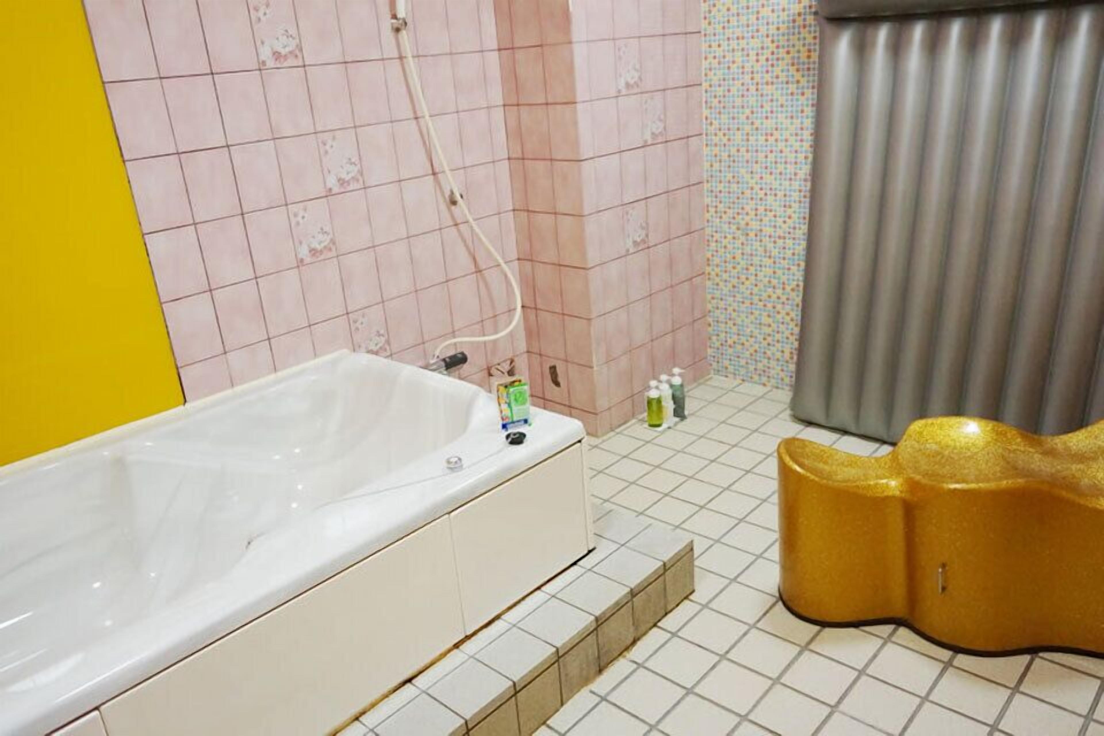 A bathroom with a white bathtub, pink patterned walls, and a yellow accent wall.