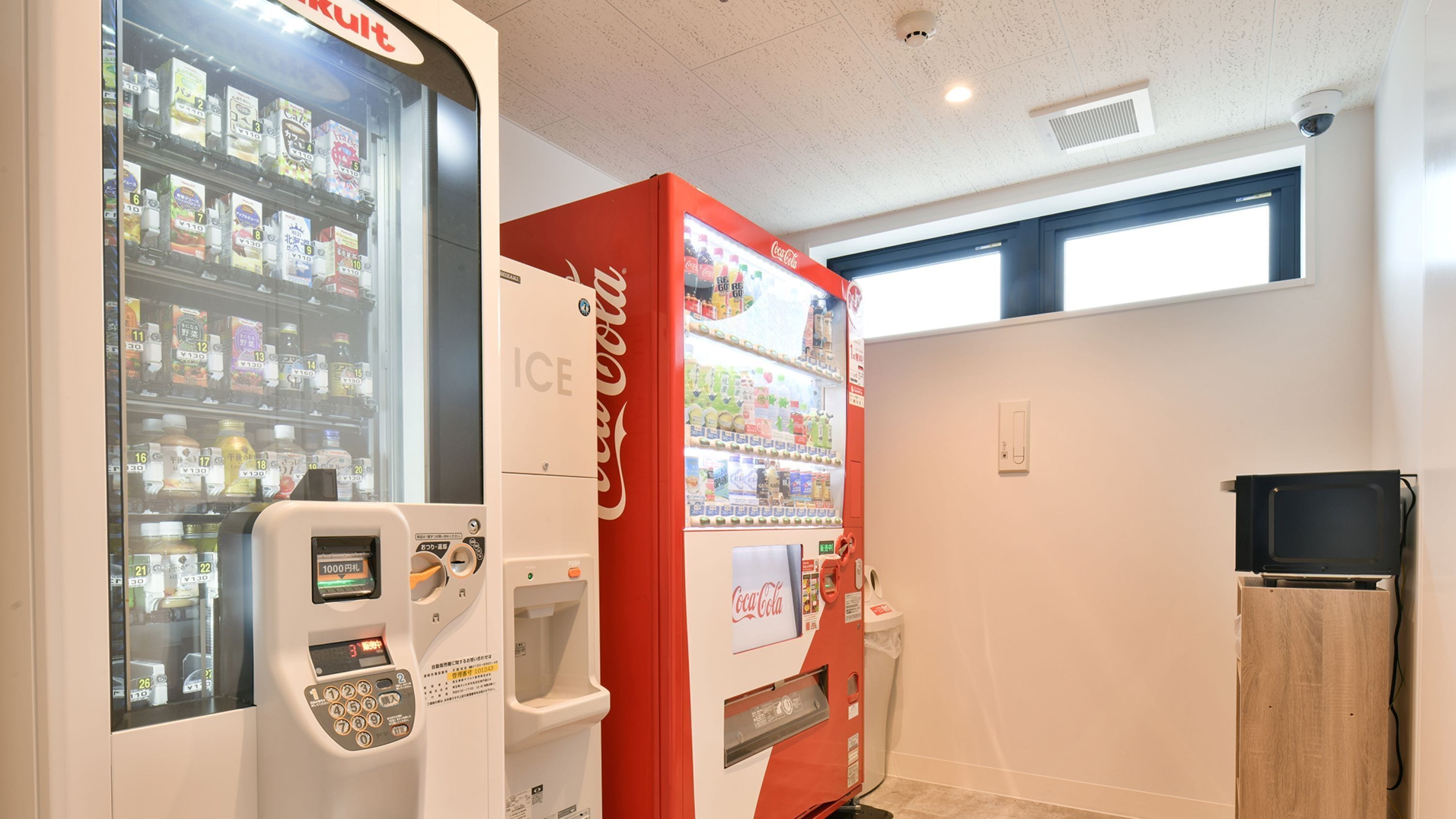 Zona con máquinas expendedoras, incluyendo una máquina de Coca-Cola y un refrigerador expositor.