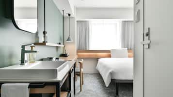 A hotel room with a bed, a desk, a chair, a sink, and a mirror.