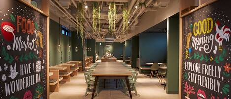 Un espacio de oficina moderno y bien iluminado con mesas largas, sillas, plantas colgantes decorativas y paredes decoradas con ilustraciones motivacionales.