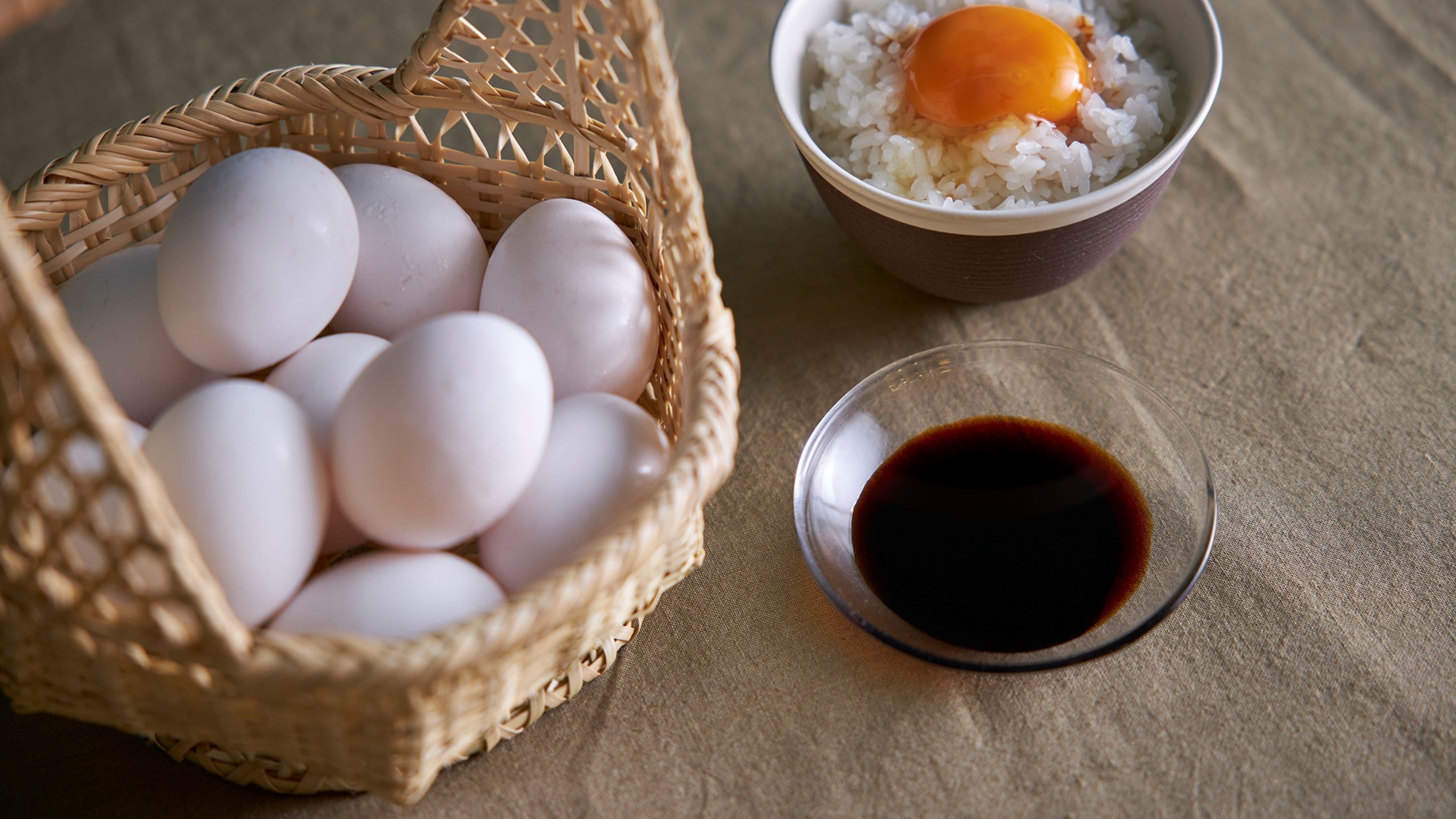 A wicker basket filled with eggs, a bowl of rice with an egg on top, and a small glass of soy sauce.