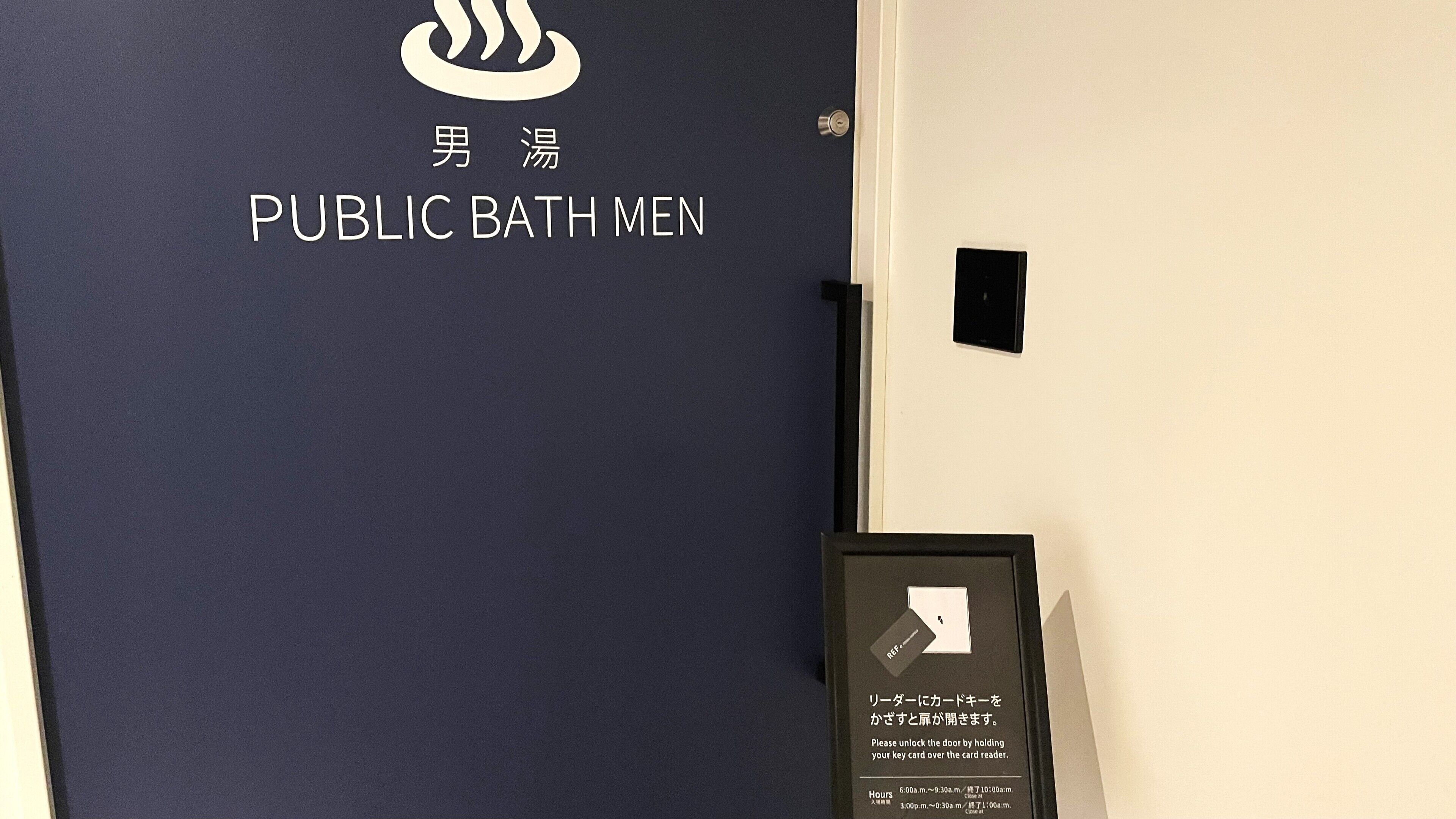 A door with a sign reading "PUBLIC BATH MEN" and instructions for unlocking the door with a key card.