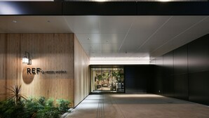 A modern hotel entrance with a wooden facade, a glass door, and a visible interior with plants and furniture. - REF Omiya by VESSEL HOTELS (Saitama)
