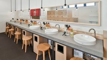 A long row of sinks with stools, a mirror, and hanging lights in a restroom.