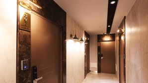 En moderne hotelgang med marmorvægge, et digitalt elevatorkontrolpanel og vægmonteret belysning.
