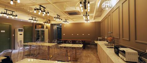 A hotel room with a long counter, multiple tables, chairs, and a ceiling with hanging lights.