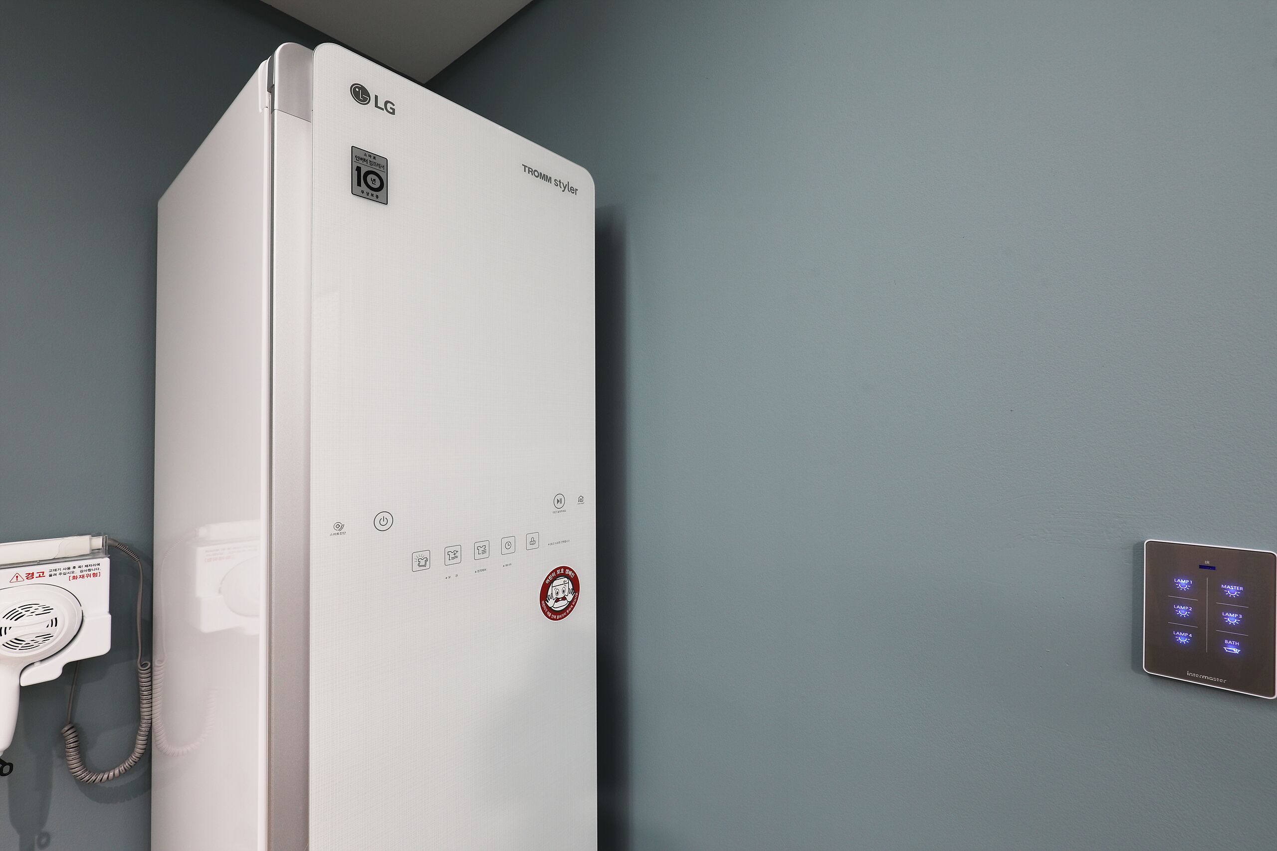 A white LG wall-mounted heater with a control panel and a thermostat on the wall.