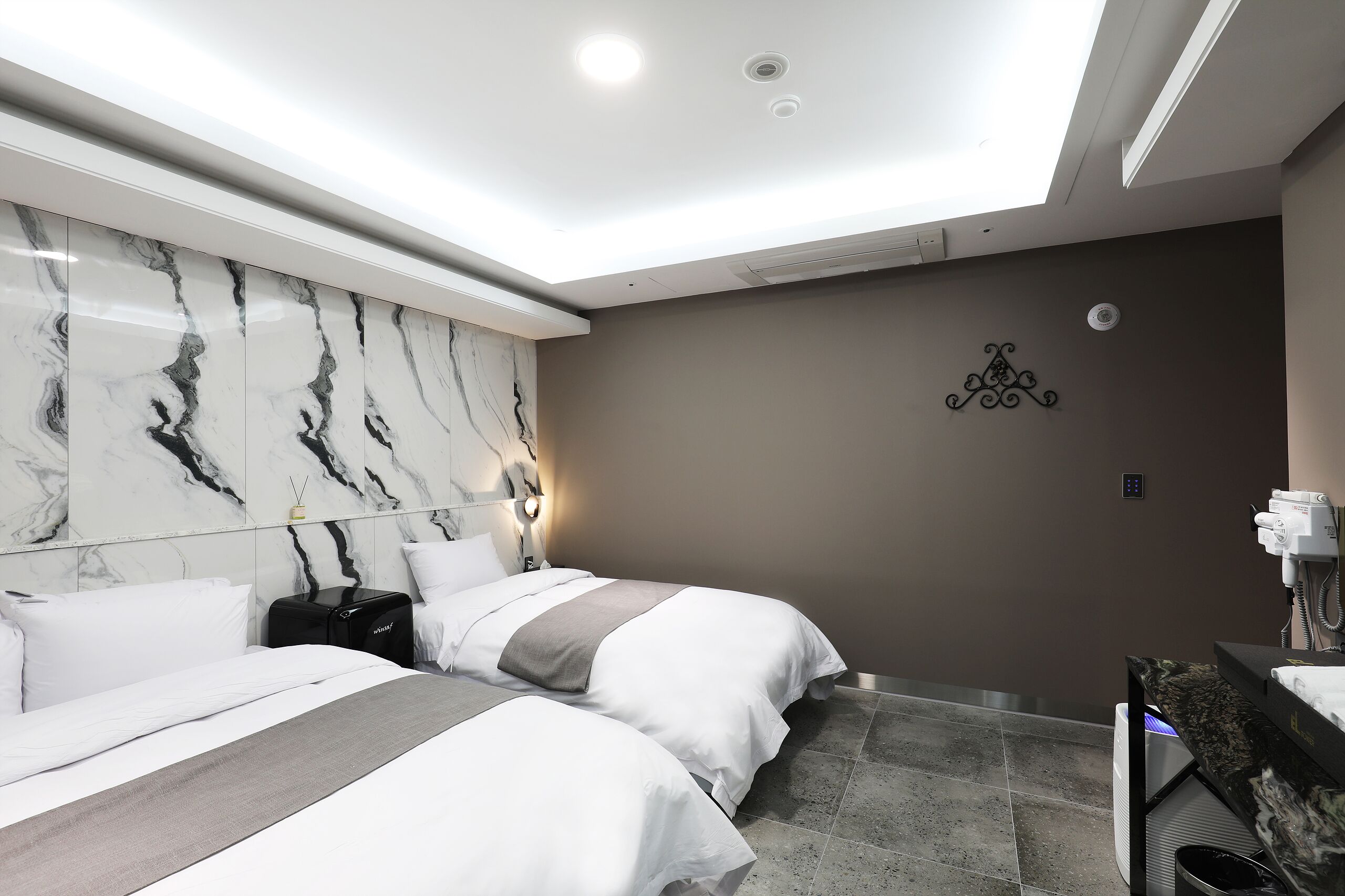 Et moderne hotelværelse med to senge, marmorvæg, loftslamper og en bordplade med marmor-mønster.