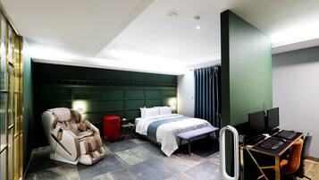 Habitación de hotel con sillón de masajes, cama con colcha azul y blanca, escritorio con ordenador y un espejo grande.