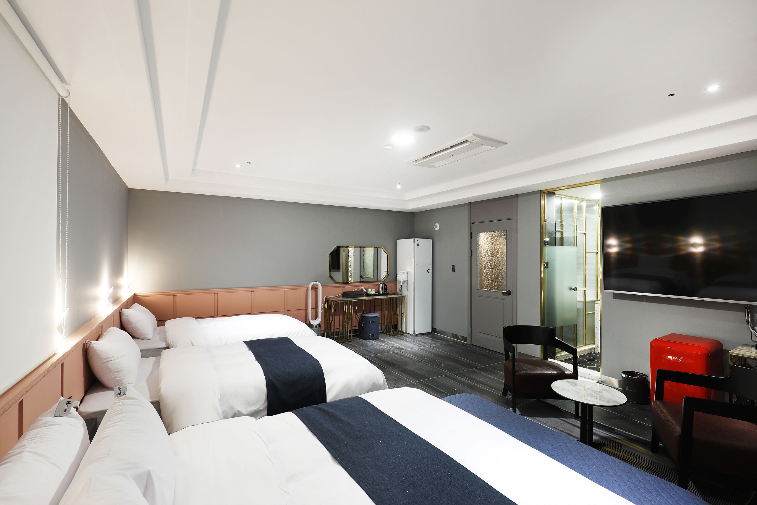 A hotel room with two beds, a desk, a chair, a TV, and a small red cabinet.
