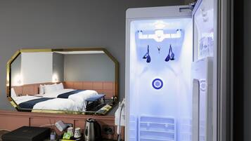 Una habitación de hotel con cama, un minibar, un espejo y un refrigerador.