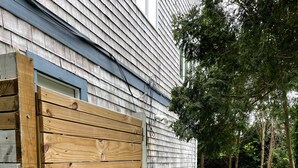A wooden gate with a black handle, a concrete pathway, and a grassy yard with trees. - Simple and clean living by the beach! (Narragansett)