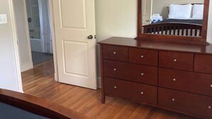 Una camera da letto con una cassettiera in legno, un letto e una porta che dà su un bagno.