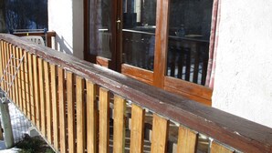 A wooden balcony with a railing, a window with a wooden frame, and a view of a snowy landscape.
