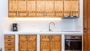 A kitchen with wooden cabinets, a stainless steel sink, and a built-in oven. - Purple Suite (Mykonos)