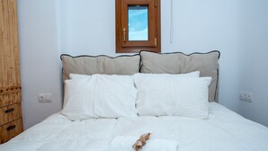 A neatly made bed with white bedding and a small window above it. - Purple Suite (Mykonos)