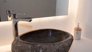 A stone sink with a modern faucet and a soap dispenser on a white countertop. - Purple Suite (Mykonos)