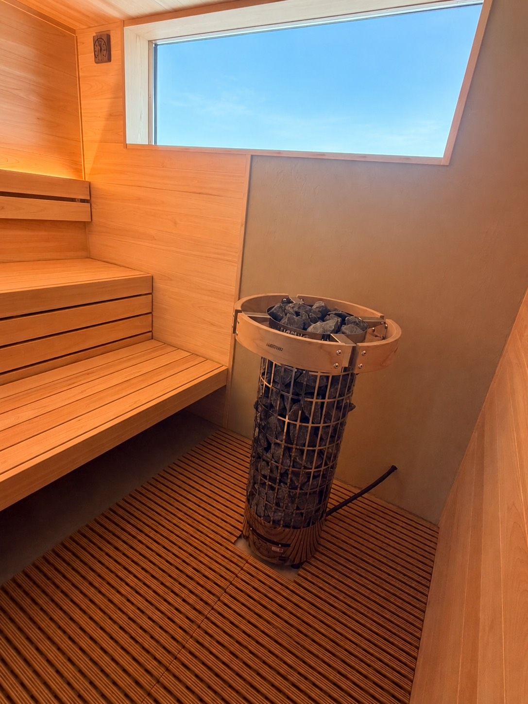 A sauna room with wooden benches, a window, and a metal ashtray.
