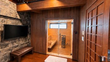 A sauna room with a wooden bench, a television mounted on a stone wall, and a sliding glass door leading to a sauna area.