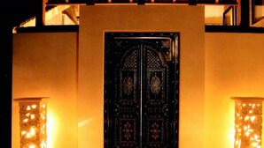 A building with a dark, ornate entrance door, flanked by two illuminated lantern-style structures. - Indigo Geohouse DS1 (Iwami)