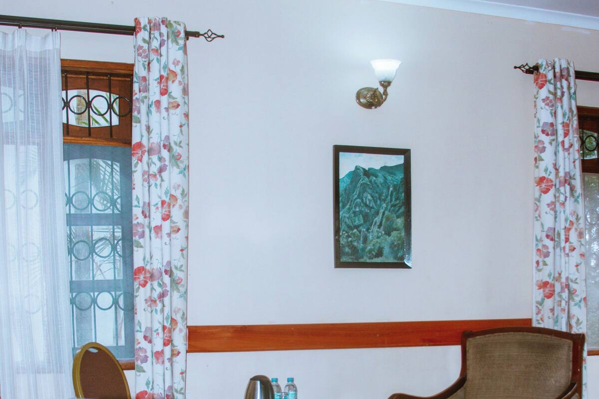 A room with a wooden desk, a chair, a laptop, a small table with a kettle, and a framed picture on the wall.