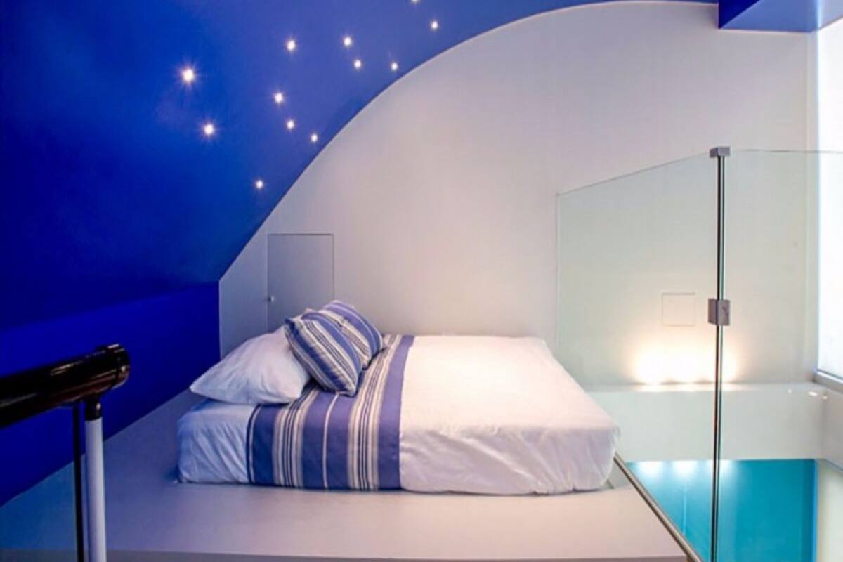 A modern bedroom with a curved ceiling, a bed with striped bedding, and a glass partition wall.