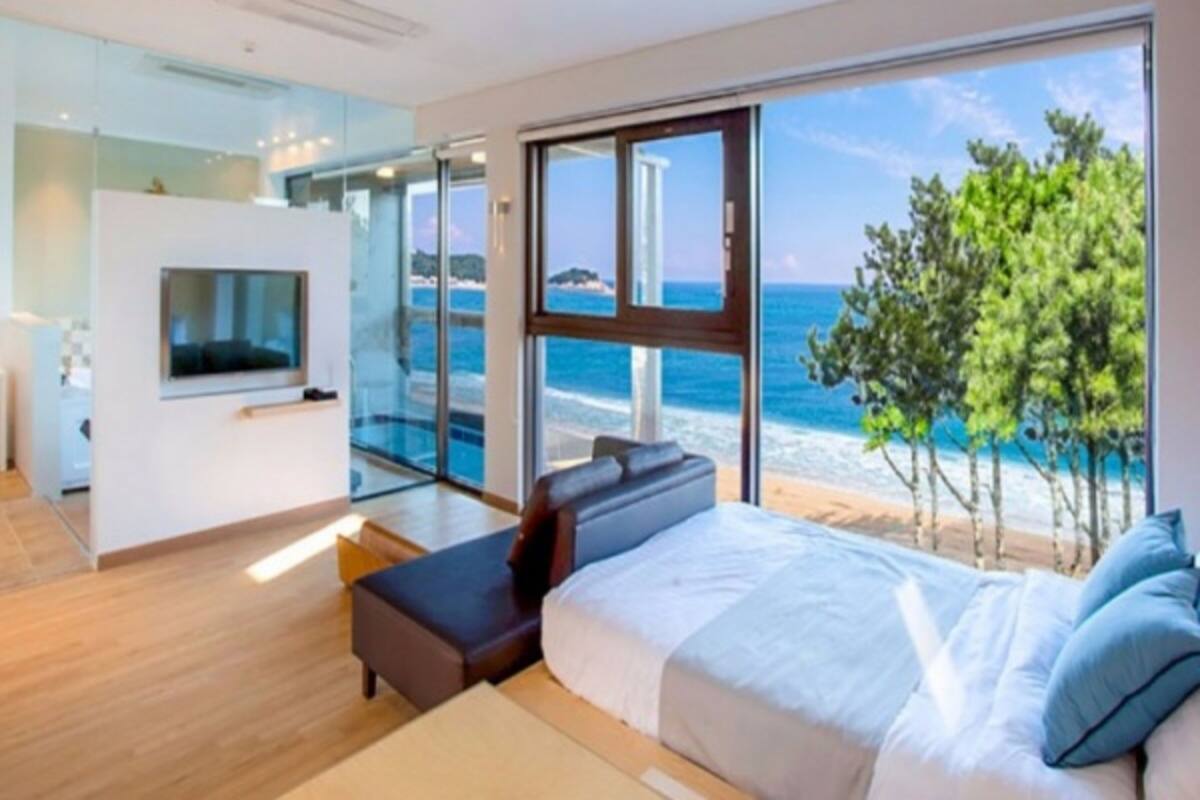 A modern bedroom with a large bed, a TV, and a view of the ocean.