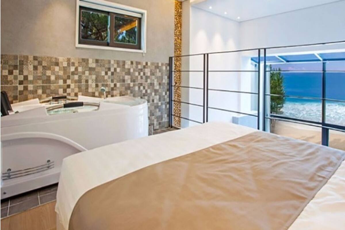 A bedroom with a large bed, a bathtub, and a view of the ocean.