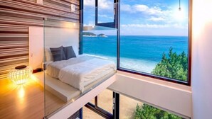 Un dormitorio moderno con una plataforma de cama de vidrio, vistas al océano y una pared de listones de madera.
