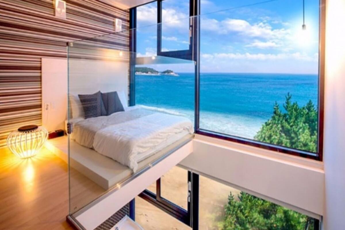 A modern bedroom with a glass bed platform, a view of the ocean, and a wooden slatted wall.