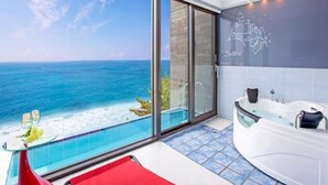 Un baño moderno con una bañera grande, ducha con cerramiento de vidrio y vistas al océano.