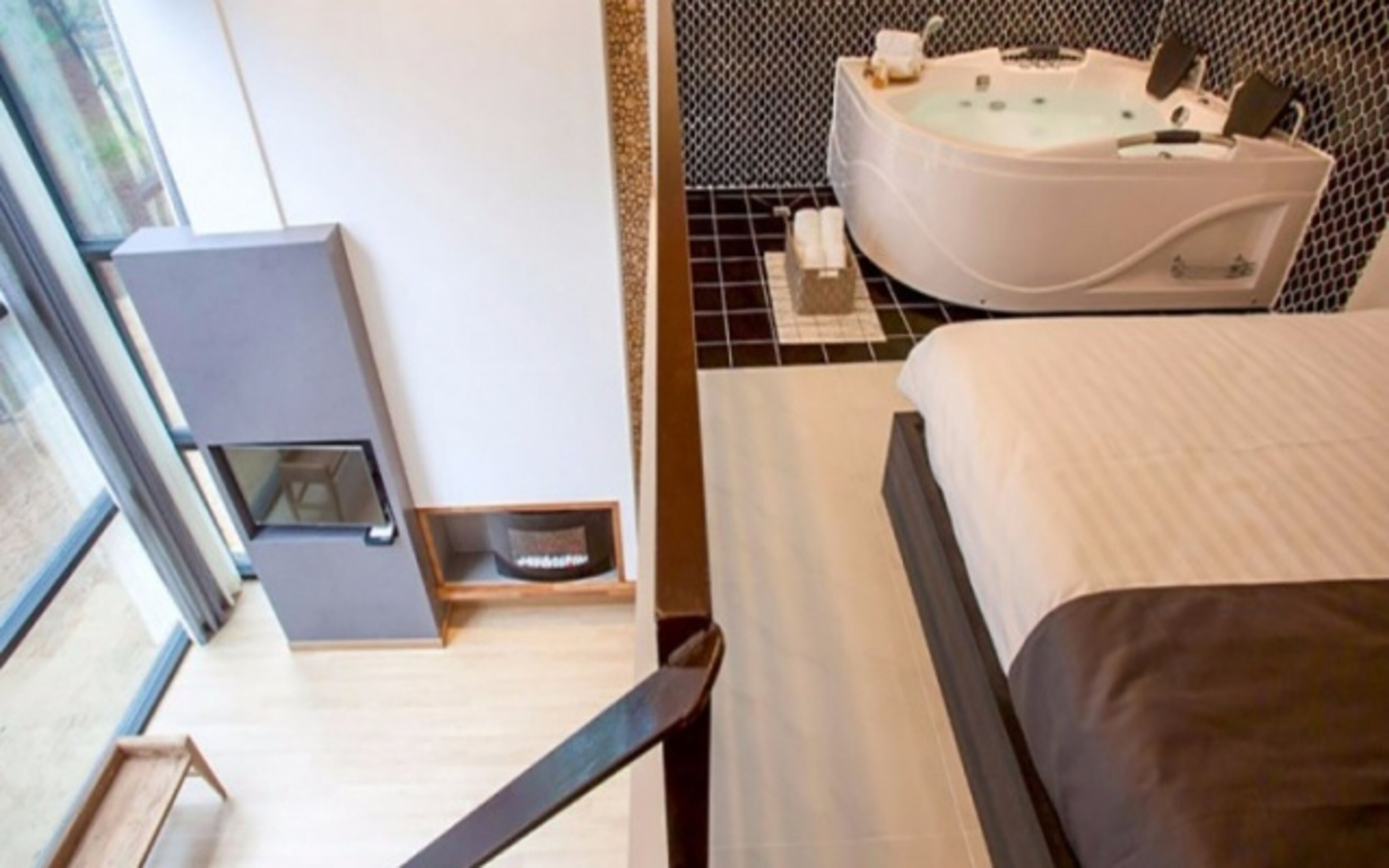 A hotel room with a bed, a small seating area, a bathtub, and a window.