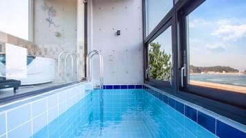Ein moderner Innenpool mit hellblauen Fliesen, einem Fenster mit Meerblick und einer weißen Badewanne.