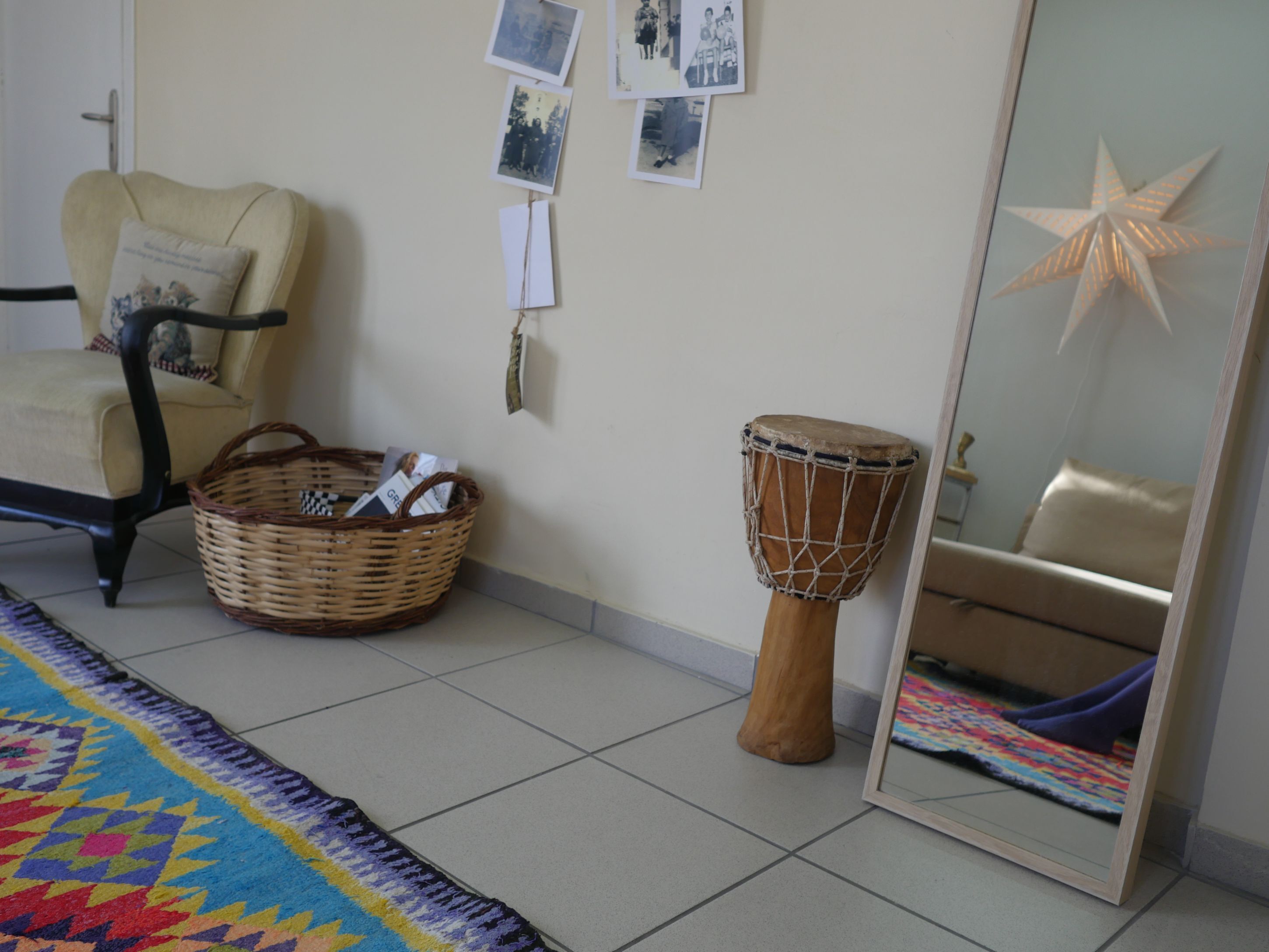 A room with a chair, a drum, a basket, and a mirror reflecting a bed.