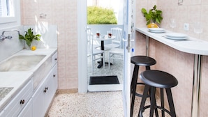 A kitchen with a sink, white cabinets, a bar area with stools, and a view of a balcony with chairs and greenery. - The Muses House (Athens)