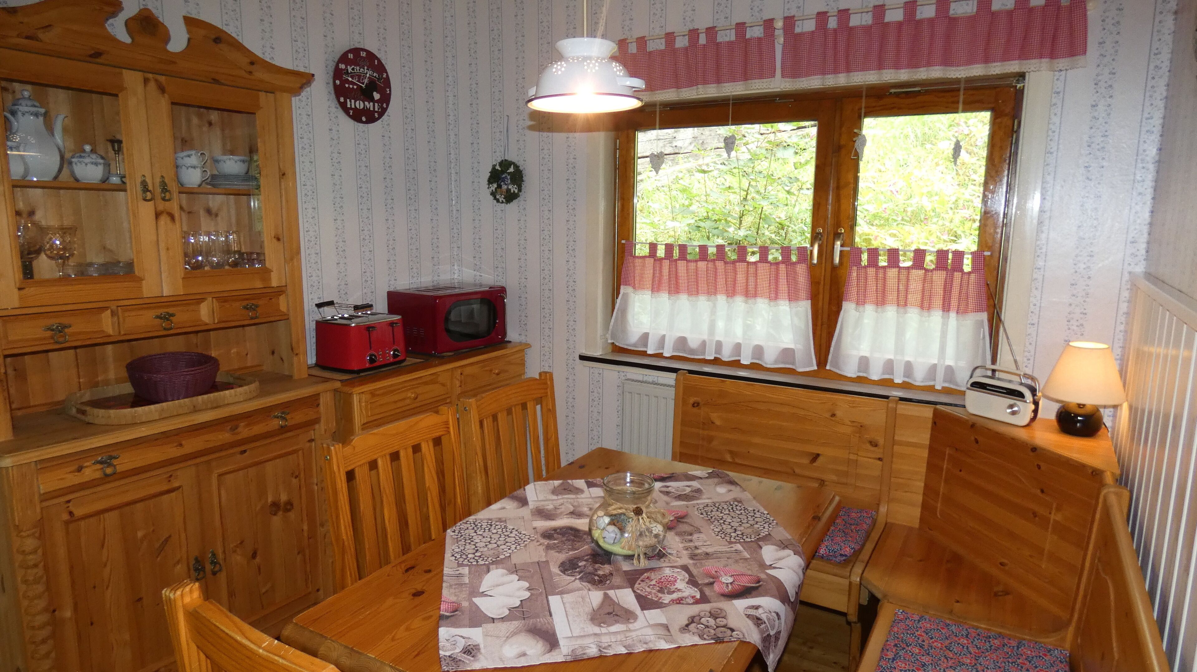 Een gezellige keuken met houten kastjes, een rode toaster, een vintage radio en een raam met gordijnen.
