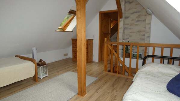A loft bedroom with a wooden staircase, a small window, and a view of the outdoors.