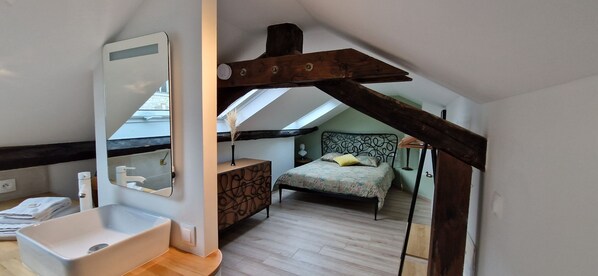 Un dormitorio con cama, mesita de noche, espejo y tragaluz.