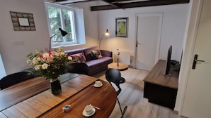 A cozy living room with a wooden dining table, a sofa, and a small side table with a vase of flowers.