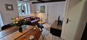 A cozy living room with a wooden dining table, a sofa, and a small side table with a vase of flowers.
