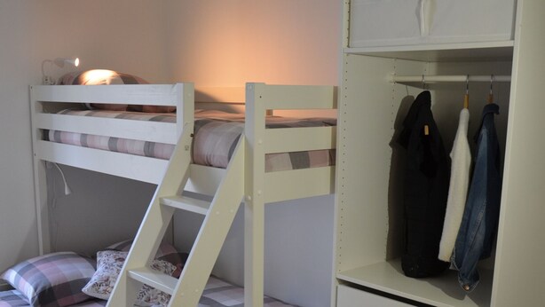 A bunk bed with a ladder, a wardrobe with hanging space, and a bedside lamp.