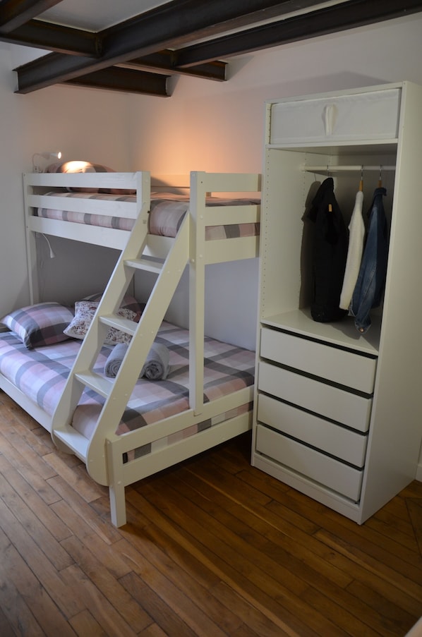 Una cama litera con escalera, un armario con espacio para colgar ropa y una lámpara de noche.